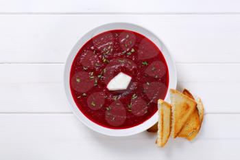 plate of beetroot cream soup with toast on white wooden background