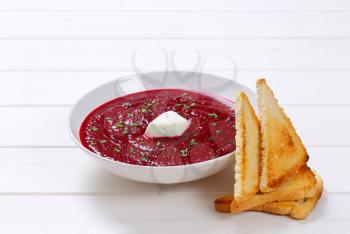 plate of beetroot cream soup with toast on white wooden background