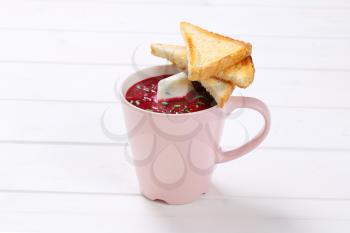 cup of beetroot cream soup with toast on white wooden background