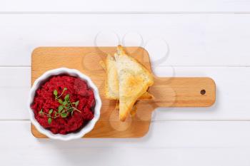 bowl of fresh beetroot puree with toast on wooden cutting board