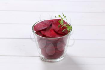 glass of thin beetroot slices on white wooden background
