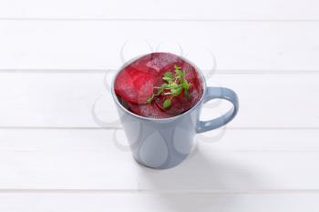cup of thin beetroot slices on white wooden background