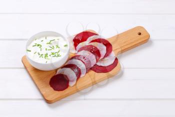 bowl of white yogurt with thin slices of beetroot and white radish on wooden cutting board