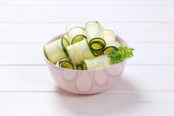 bowl of raw zucchini strips on white wooden background