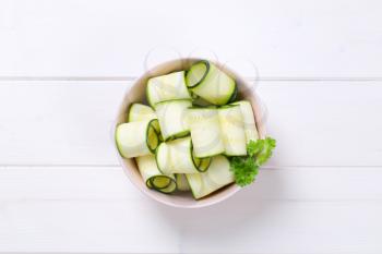 bowl of raw zucchini strips on white wooden background