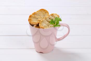 cup of crispy rusks on white wooden background