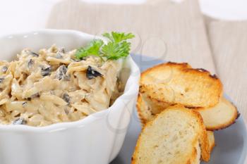 bowl of grated cheese spread with olives and crostini on grey plate - close up