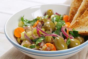bowl of vegetable salad with pickled green olives and toast on beige place mat - close up
