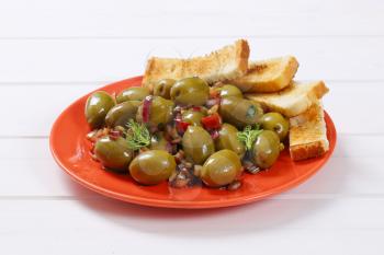 plate of marinated green olives with toast on white wooden background