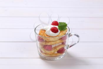 cup of american pancakes with white yogurt and fresh raspberries on white wooden background