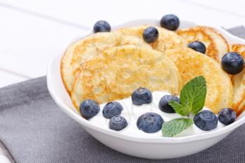 bowl of american pancakes with white yogurt and fresh blueberries on grey place mat - close up