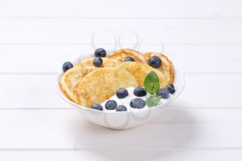 bowl of american pancakes with white yogurt and fresh blueberries on white wooden background
