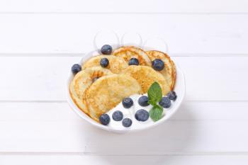 bowl of american pancakes with white yogurt and fresh blueberries on white wooden background