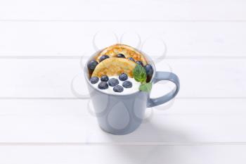 cup of american pancakes with white yogurt and fresh blueberries on white wooden background