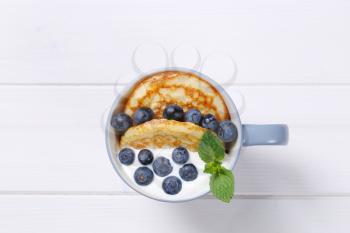 cup of american pancakes with white yogurt and fresh blueberries on white wooden background