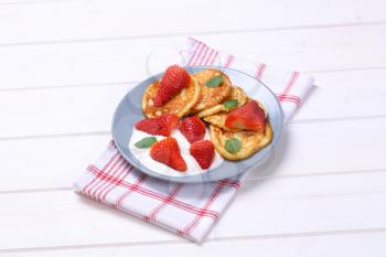 plate of american pancakes with white yogurt and fresh strawberries on checkered dishtowel