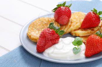 plate of american pancakes with white yogurt and fresh strawberries on blue place mat - close up