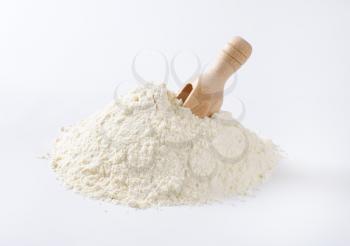 pile of wheat flour and wooden scoop on white background