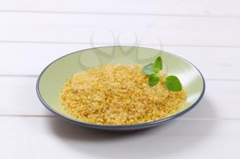 plate of dry wheat bulgur on white wooden background