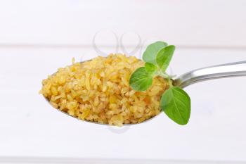 spoon of dry wheat bulgur on white wooden background
