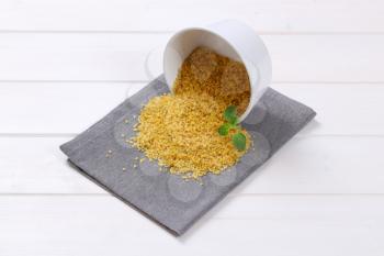 bowl of dry wheat bulgur spilt out on grey place mat