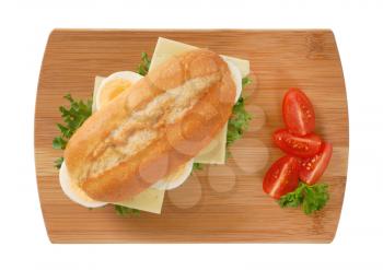 crusty roll sandwich with eggs and cheese on wooden cutting board