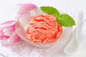 Scoop of pink fruit flavored ice cream in bowl
