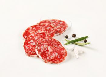 slices of French dry cured salami with spices on white background