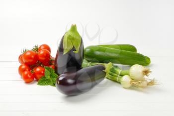 fresh eggplants, tomatoes, zucchini and spring onion on white wooden background