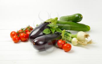 fresh eggplants, tomatoes, zucchini and spring onion on white wooden background