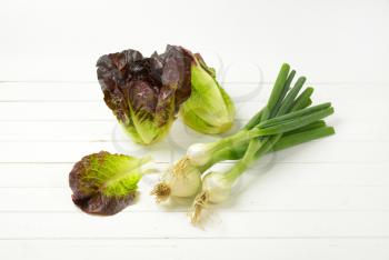 bunch of spring onions and heads of fresh lettuce on white wooden background