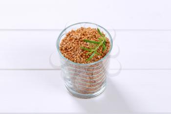 glass of raw buckwheat on white wooden background