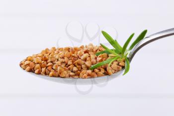 spoon of raw buckwheat on white wooden background