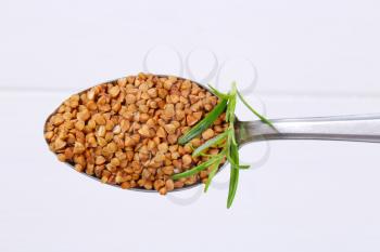 spoon of raw buckwheat on white wooden background