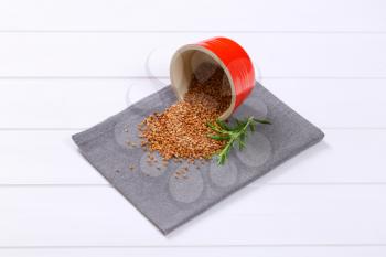 bowl of raw buckwheat spilt out on grey place mat