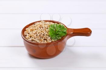 saucepan of cooked pearl barley on white wooden background