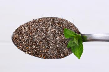 spoon of chia seeds on white wooden background