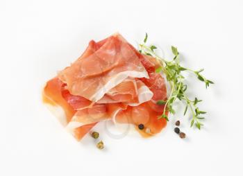 slices of air dried ham with thyme and pepper on white background