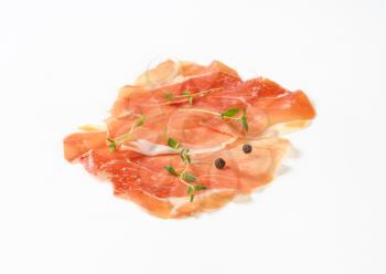 slices of air dried ham with thyme and pepper on white background