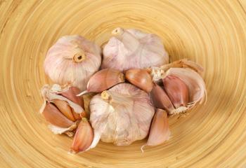 bulbs and cloves of fresh garlic on wooden plate - close up