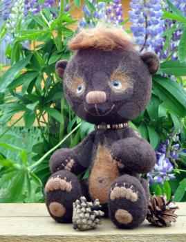 Handmade, the sewed toy: teddy-bear Mocca on a little board among flowers lupine and buttercups