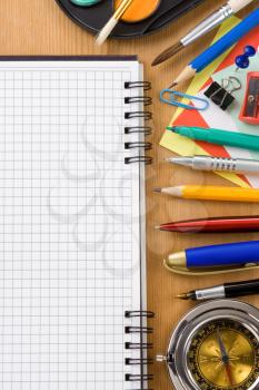 school supplies and checked notebook on wood background