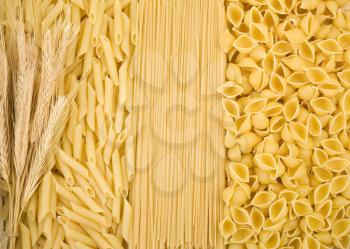 raw pasta and ear of wheat as background