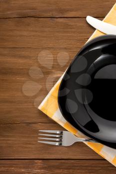 plate, knife and fork at napkin on wooden background