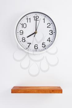 wall clock at wooden shelf on white background