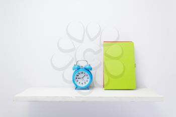 notepad and alarm clock on shelf at white background surface