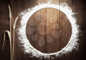 flour powder and wheat ears on wooden background
