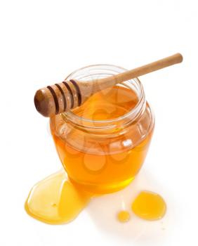 glass jar full of honey and dipper isolated on white background