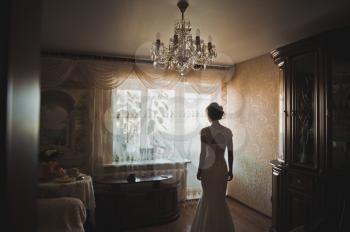 The bride in a wedding dress is by the window.