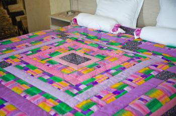 Blanket on a bed from bright pieces of a fabric.